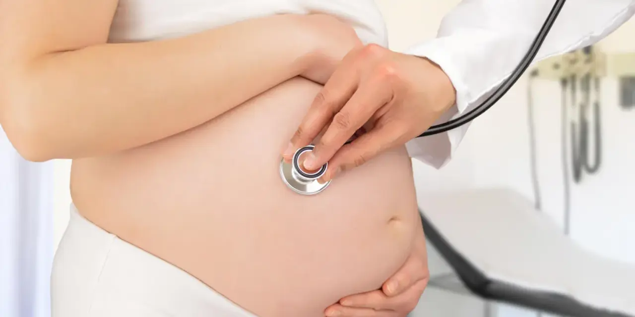 Visita medica per monitorare la gravidanza. Il medico ascolta il battito cardiaco del feto con uno stetoscopio sul pancione.