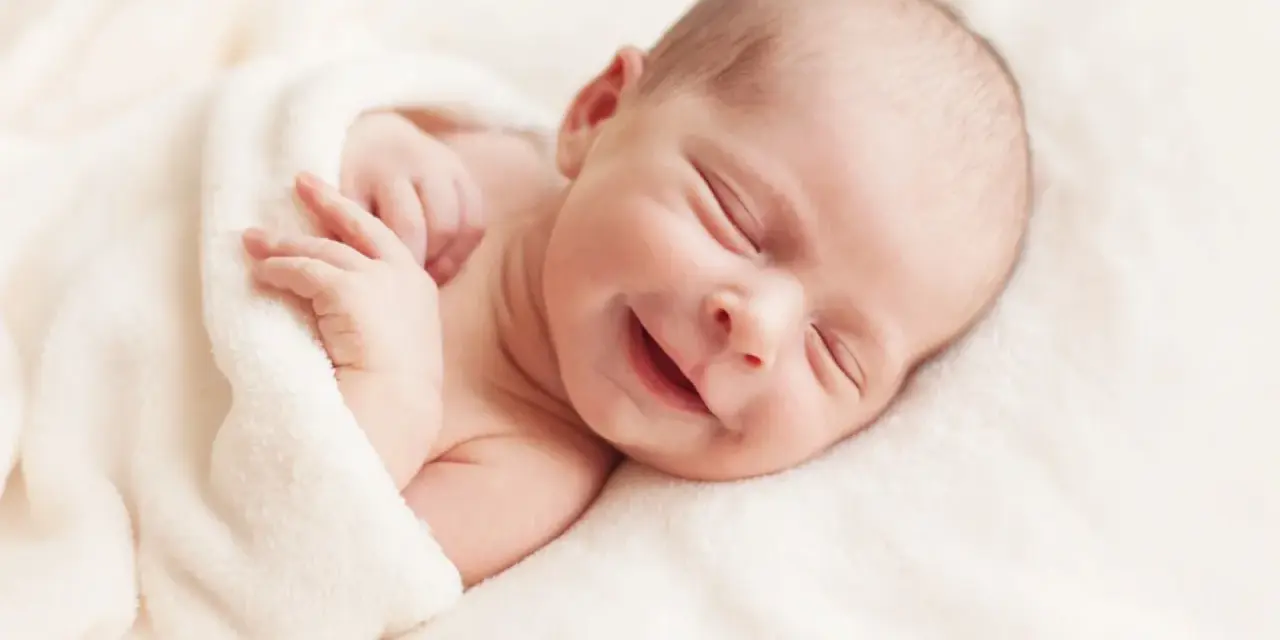 Un adorabile neonato non dorme, ma sorride beatamente avvolto in una coperta morbida.