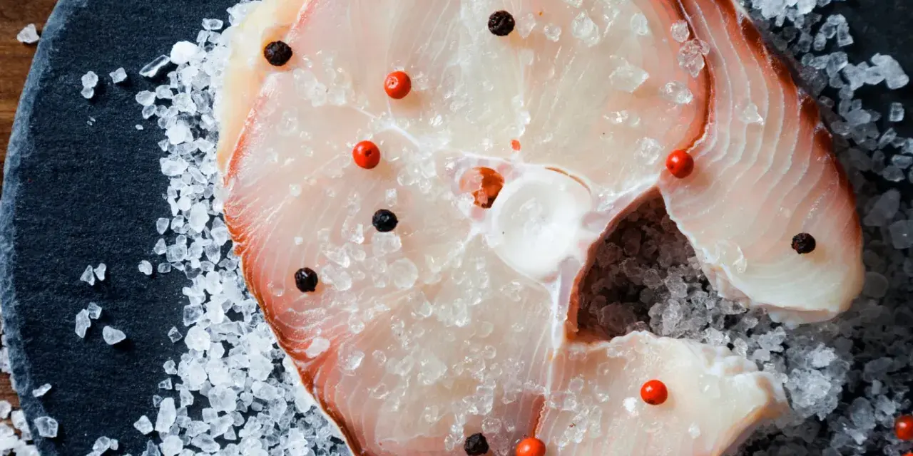 Raw swordfish steak with salt and peppercorns on a dark slate.