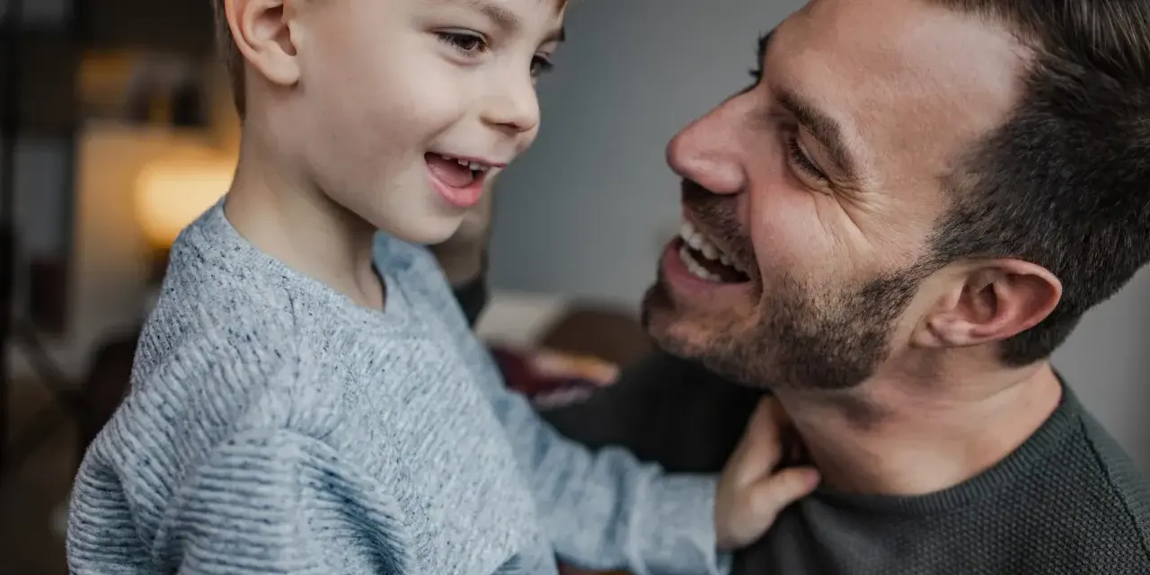 Un padre e suo figlio ridono guardandosi negli occhi. Il bambino, con un maglione grigio, sembra chiedere "perché mio figlio non mi chiama mamma?".