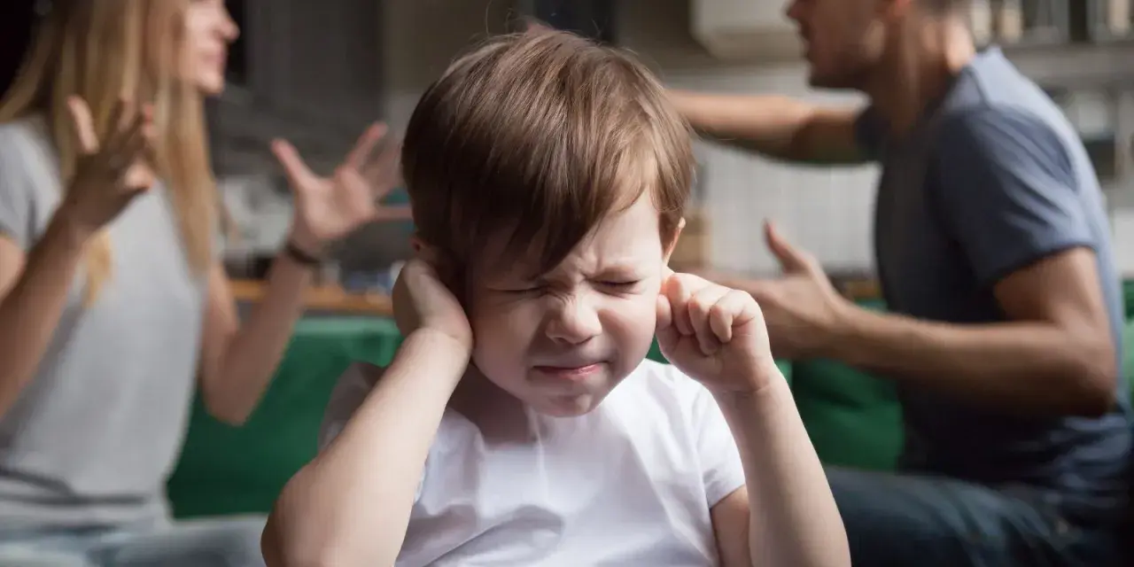 Bambino con le mani sulle orecchie, mentre i genitori litigano. Una scena che mostra una crisi di coppia con figli.