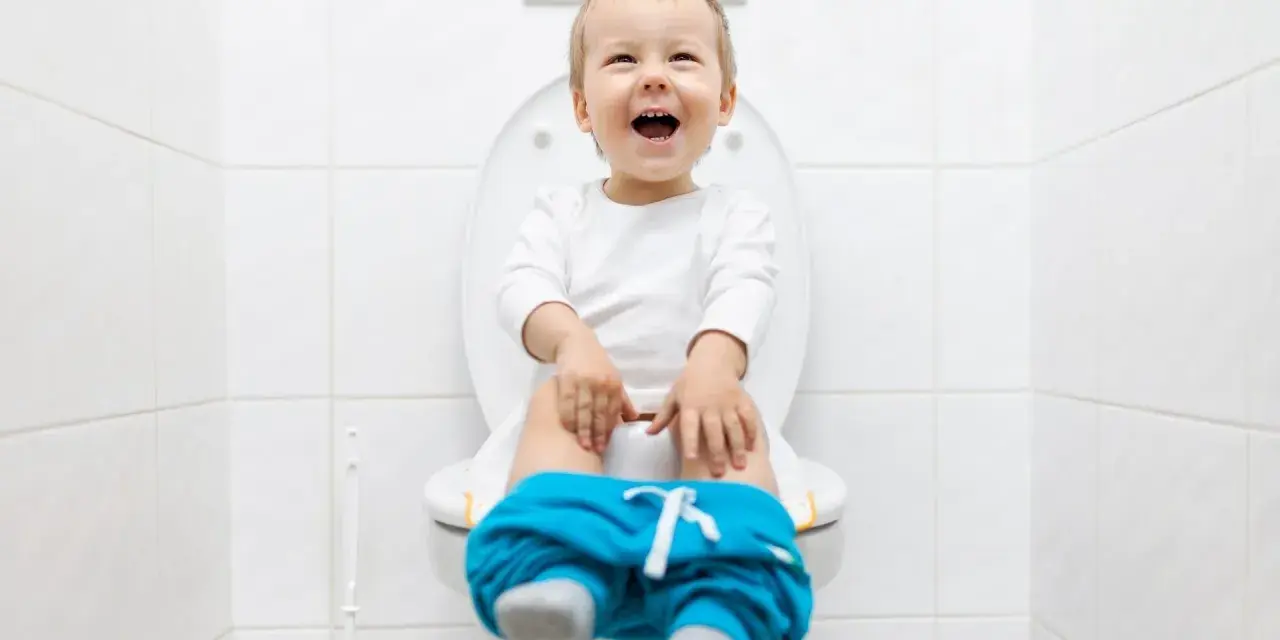 Bambino felice sul water, pantaloni abbassati, pronto per fare la cacca.