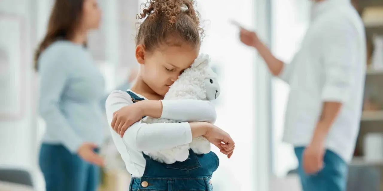 Bambina abbraccia peluche, turbata dalle liti dei genitori separati.