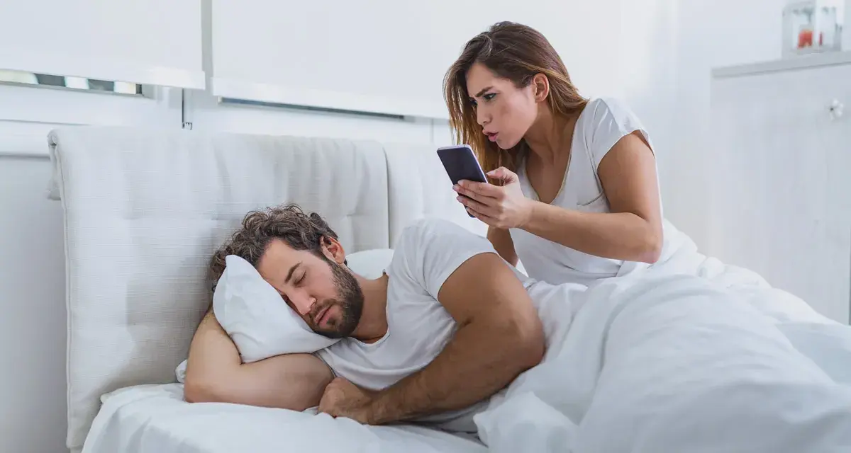 Donna guarda il telefono con sorpresa mentre il marito dorme. Sembra che mio marito abbia sempre il telefono in mano, anche a letto!