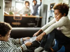 Bambini litigano per un tablet, un classico esempio di gelosia tra fratelli. In cucina, i genitori sembrano ignari.