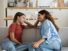 Madre e figlia si guardano sorridendo sul divano. La figlia, con un bottone mammario a 7 anni, ascolta attenta.