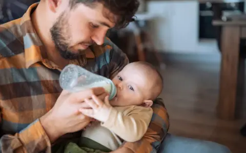 Padre con barba nutre il neonato con il biberon. Scopri trucchi per far prendere il biberon al tuo piccolo.