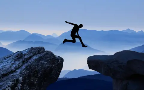 Silhouette di una persona che salta tra due rocce, con montagne blu sullo sfondo. Un viaggio per perdersi per ritrovarsi, un salto nel vuoto per una coppia.