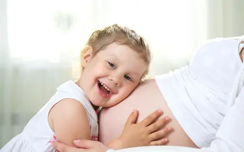 Bambina di 3 anni felice abbraccia la pancia della mamma, in attesa dell'arrivo di un fratellino.