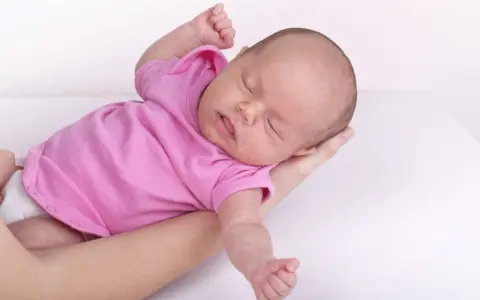 Neonato in rosa si irrigidisce e stringe i pugni, dormendo sereno tra le braccia.