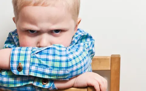 Bambino di 20 mesi ingestibile, con sguardo corrucciato e braccia incrociate sulla sedia.