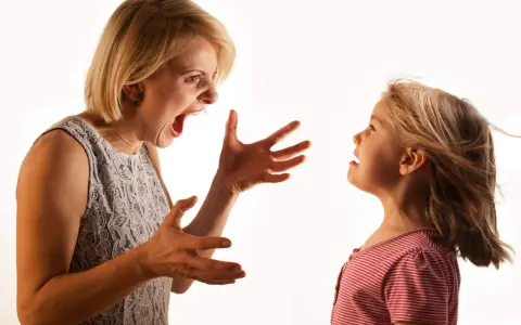 Una madre sgrida il figlio con veemenza, le mani aperte in un gesto di rimprovero. La bambina la guarda, visibilmente scossa.