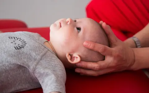Un neonato sbatte la testa sul petto, con mani adulte che lo sostengono delicatamente.