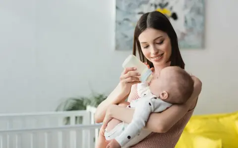 Mamma sorridente nutre il neonato con latte artificiale. Il piccolo potrebbe avere cacca liquida, ma ora è felice.