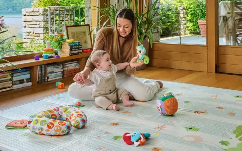 Mamma gioca con un neonato di 6 mesi che non sta seduto, su un tappeto gioco con tanti giocattoli colorati.