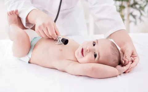 Un neonato sorride mentre il pediatra ascolta il suo respiro con uno stetoscopio.