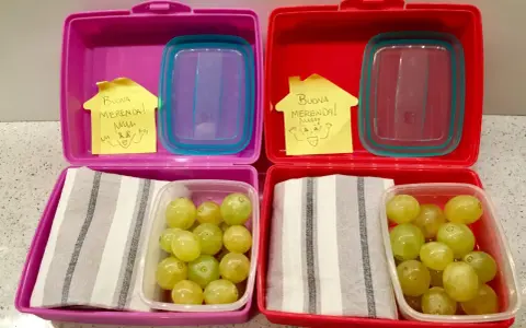 Due lunchbox rosa e rosse pronte per le merende per bambini, con uva e un bigliettino "Buona Merenda!".