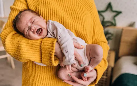 Neonato di 11 mesi con scatti nervosi, piange tra le braccia di chi lo tiene, avvolto in un maglione giallo.