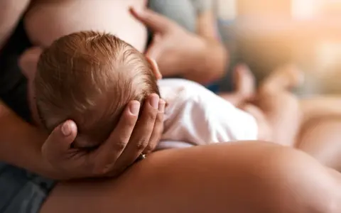 Un neonato si nutre al seno, la sua testolina è tenuta da una mano. La montata lattea non arriva, ma l'amore è presente.