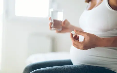 Donna incinta tiene una pillola e un bicchiere d'acqua. L'uso di cortisone in gravidanza va valutato attentamente.