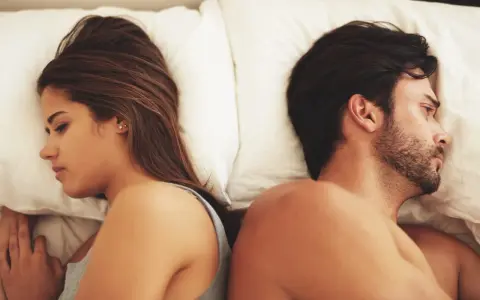 Coppia a letto, schiena contro schiena, con espressioni pensierose. Un'immagine che fa riflettere su come capire se una relazione è finita.