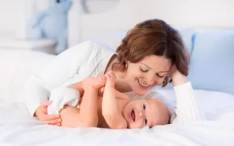 Mamma sorride mentre gioca con il suo neonato, svegliandolo dolcemente per mangiare.