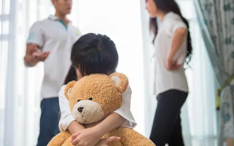 Bambina abbraccia orsacchiotto, mentre i genitori discutono. Avere coraggio di separarsi è difficile per tutti.