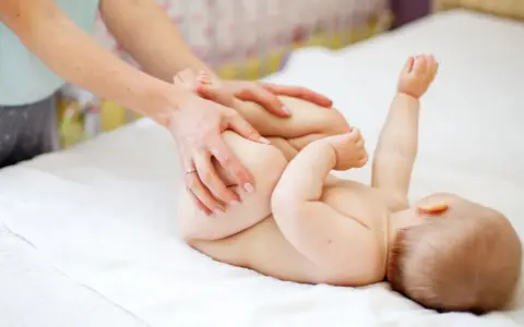 Mani che aiutano il neonato a fare la cacca con movimenti delicati sulle gambine.