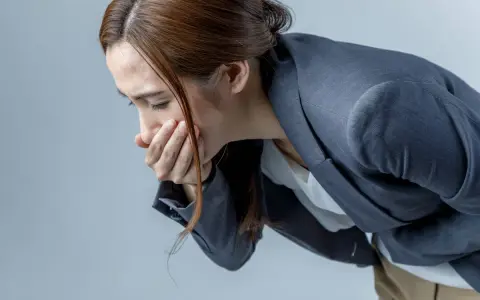 Donna con la mano sulla bocca, visibilmente sofferente, con la paura di vomitare.