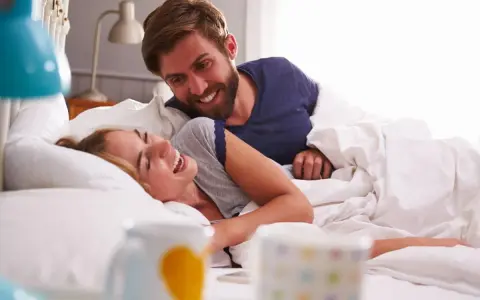 Coppia sorridente a letto, un momento di gioia che va oltre i rapporti promiscui, un legame profondo.