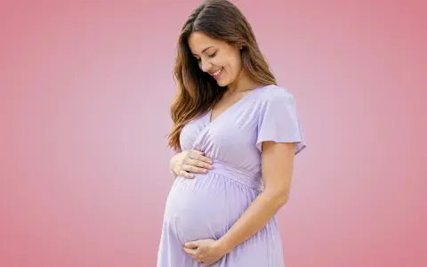 Donna incinta sorride, accarezzando il pancione. Importante assumere acido folico prima o dopo i pasti per la salute del bambino.