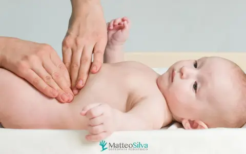Mani che massaggiano la pancia di un neonato, forse per alleviare coliche o cacca acida. Un momento di cura per i più piccoli.