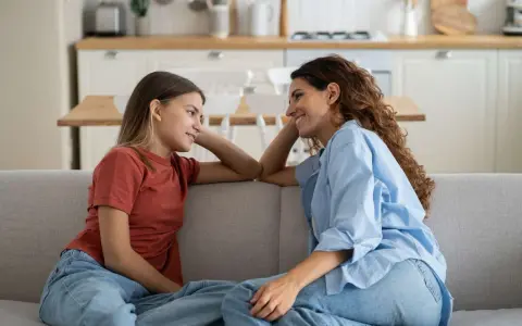 Madre e figlia si guardano sorridendo sul divano. La figlia, con un bottone mammario a 7 anni, ascolta attenta.