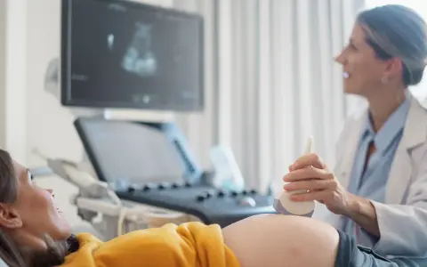 Ecografia di una donna incinta, con il medico che usa la sonda per sentire il battito del feto. L'emozione sul volto della futura mamma è palpabile.