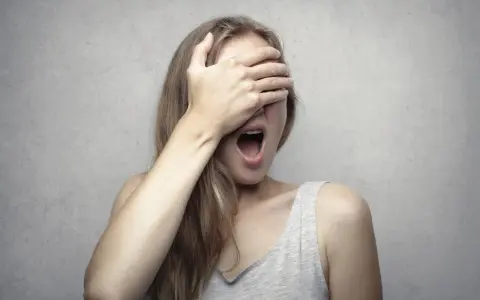Ragazza con la mano sugli occhi, bocca spalancata, forse per la fobia del vomito (emetofobia).