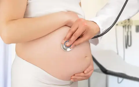 Visita medica per monitorare la gravidanza. Il medico ascolta il battito cardiaco del feto con uno stetoscopio sul pancione.