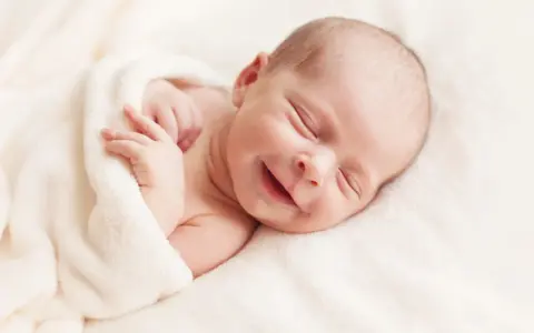 Un adorabile neonato non dorme, ma sorride beatamente avvolto in una coperta morbida.