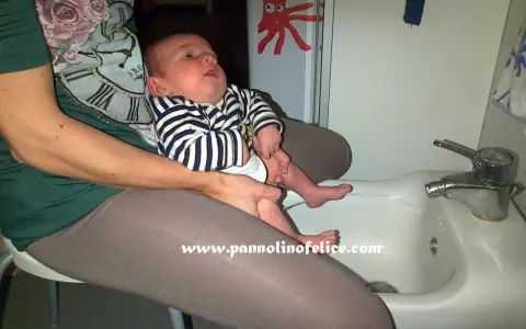 Un bimbo fa pipì in giro mentre è seduto sul lavandino, con un adesivo di polpo sul muro.