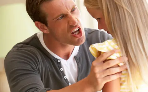 Un uomo arrabbiato urla contro una bambina. La sua espressione facciale è feroce, con gli occhi stretti e la bocca spalancata. La bambina, con i capelli biondi lunghi, sembra spaventata e si ritrae. La scena evoca un senso di tensione e conflitto famil...