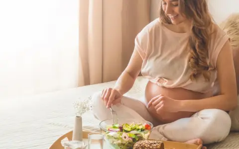 Donna incinta sorride mangiando un'insalata fresca. Il burro in gravidanza è un alimento importante per la crescita del feto.