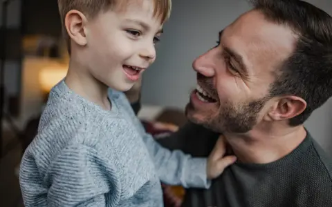 Un padre e suo figlio ridono guardandosi negli occhi. Il bambino, con un maglione grigio, sembra chiedere "perché mio figlio non mi chiama mamma?".