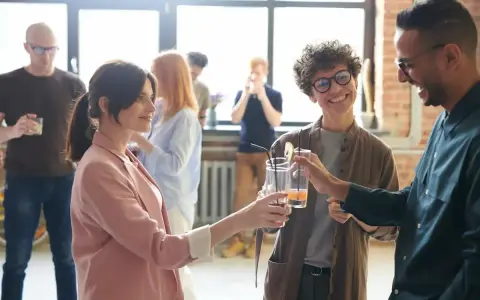 Persone brindano con drink, i loro occhi che si incrociano trasmettono un'ansia sottile, ma anche speranza.