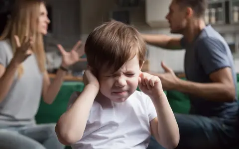 Bambino con le mani sulle orecchie, mentre i genitori litigano. Una scena che mostra una crisi di coppia con figli.