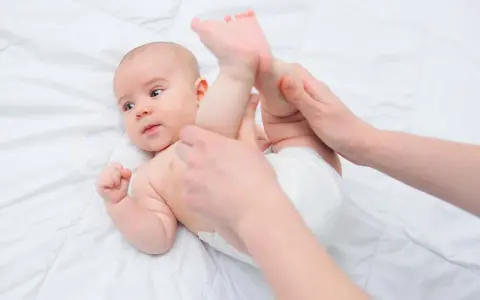 Mani che aiutano un neonato a liberarsi dall'aria nella pancia, con le gambine sollevate delicatamente.