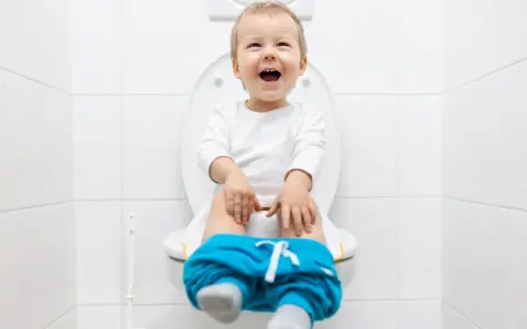 Bambino felice sul water, pantaloni abbassati, pronto per fare la cacca.
