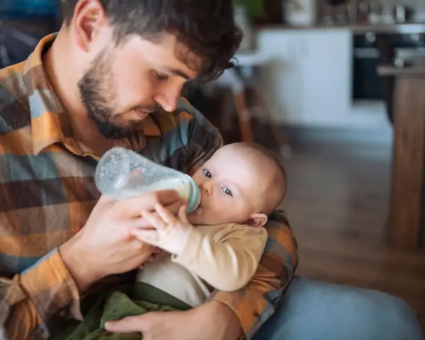 Padre con barba nutre il neonato con il biberon. Scopri trucchi per far prendere il biberon al tuo piccolo.