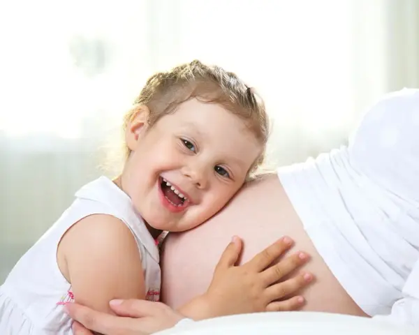 Bambina di 3 anni felice abbraccia la pancia della mamma, in attesa dell'arrivo di un fratellino.