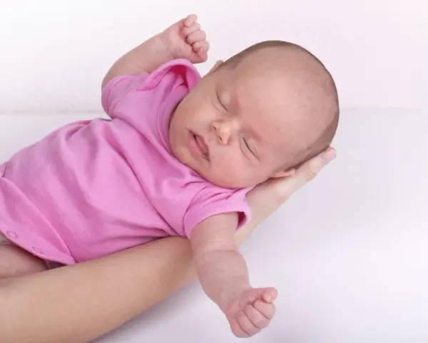 Neonato in rosa si irrigidisce e stringe i pugni, dormendo sereno tra le braccia.