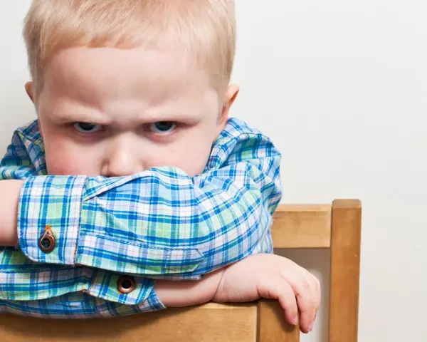 Bambino di 20 mesi ingestibile, con sguardo corrucciato e braccia incrociate sulla sedia.
