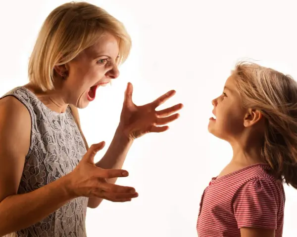 Una madre sgrida il figlio con veemenza, le mani aperte in un gesto di rimprovero. La bambina la guarda, visibilmente scossa.